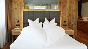 Una cama grande con cabecera tapizada de gris, dos mesitas de noche con lámparas y un armario de madera.