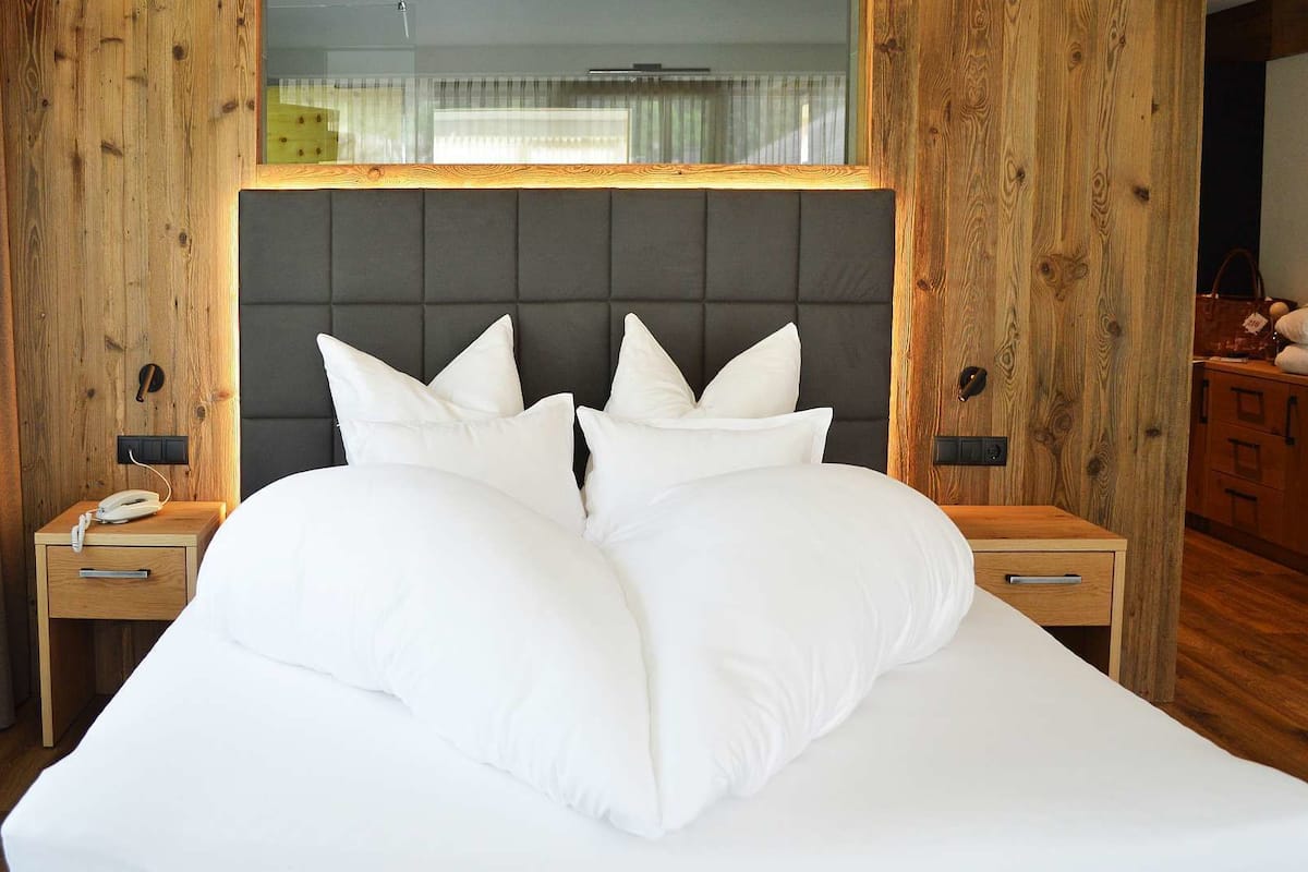 A large bed with a grey upholstered headboard, two bedside tables with lamps, and a wooden wardrobe.