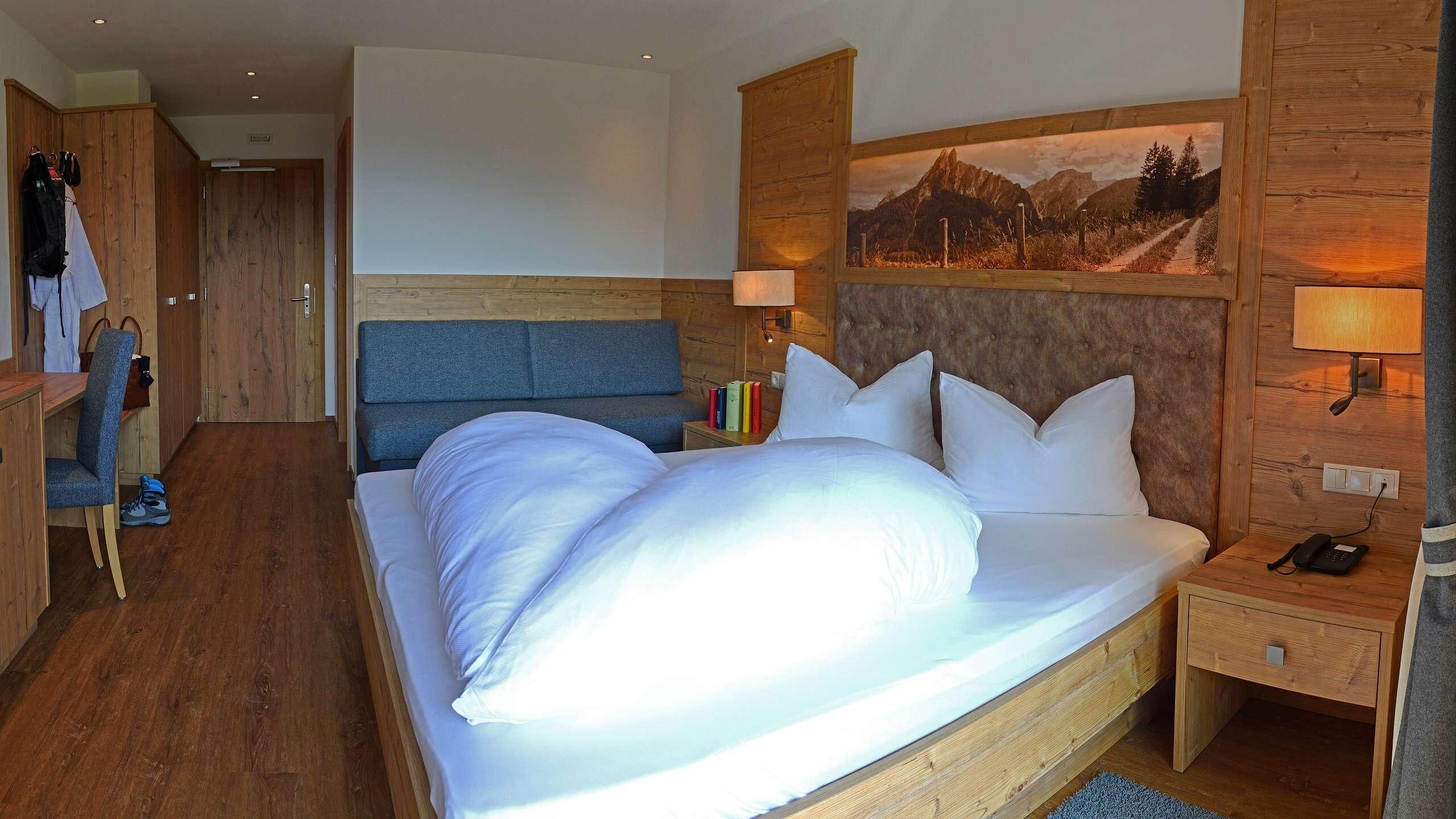 A hotel room with a large bed, a desk, a chair, and a wardrobe.