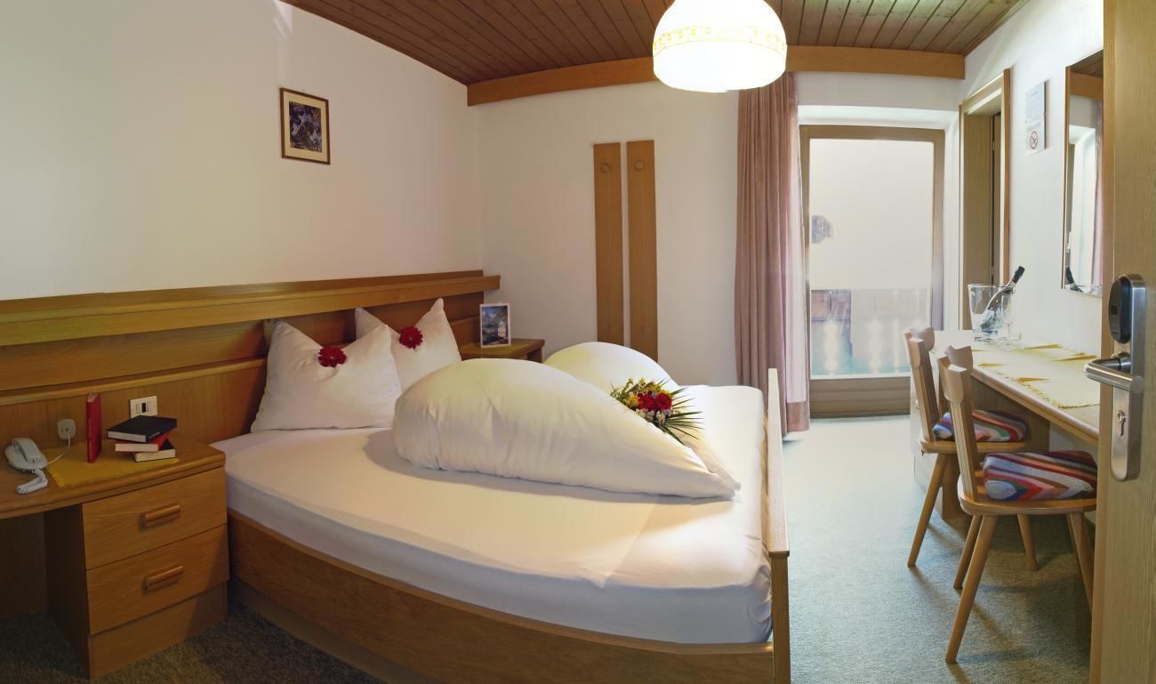 A hotel room with a wooden bed, bedside table, and a desk with chairs.