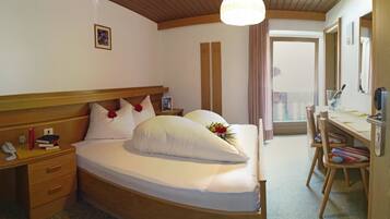 A hotel room with a wooden bed, bedside table, and a desk with chairs.