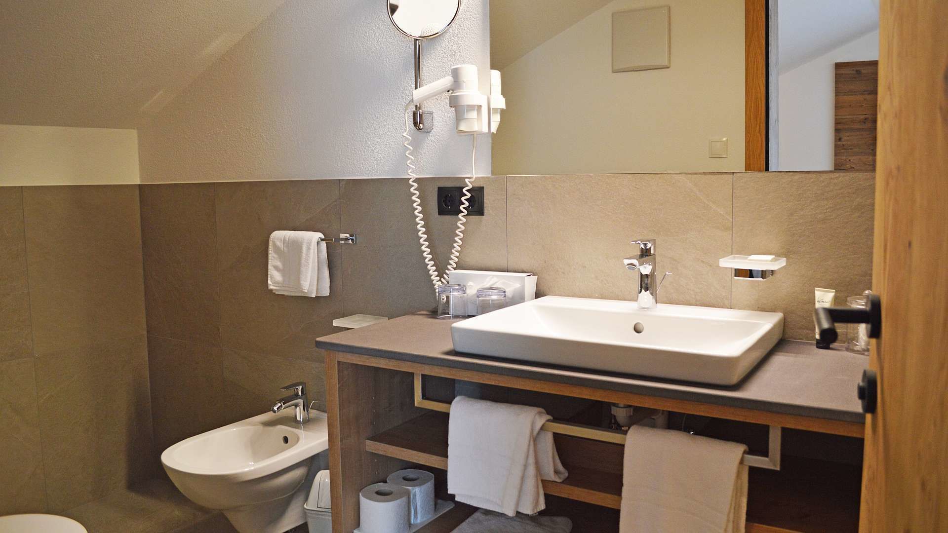 Un baño moderno con un lavabo grande, un bidé y un espejo. Hay toallas y artículos de aseo en la encimera.
