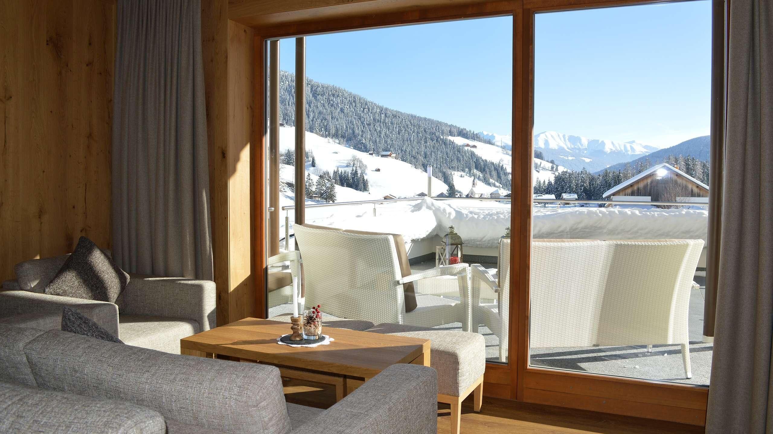 Una habitación acogedora con un amplio ventanal que ofrece vistas a una montaña nevada. Hay un sofá y una pequeña mesa con una vela.