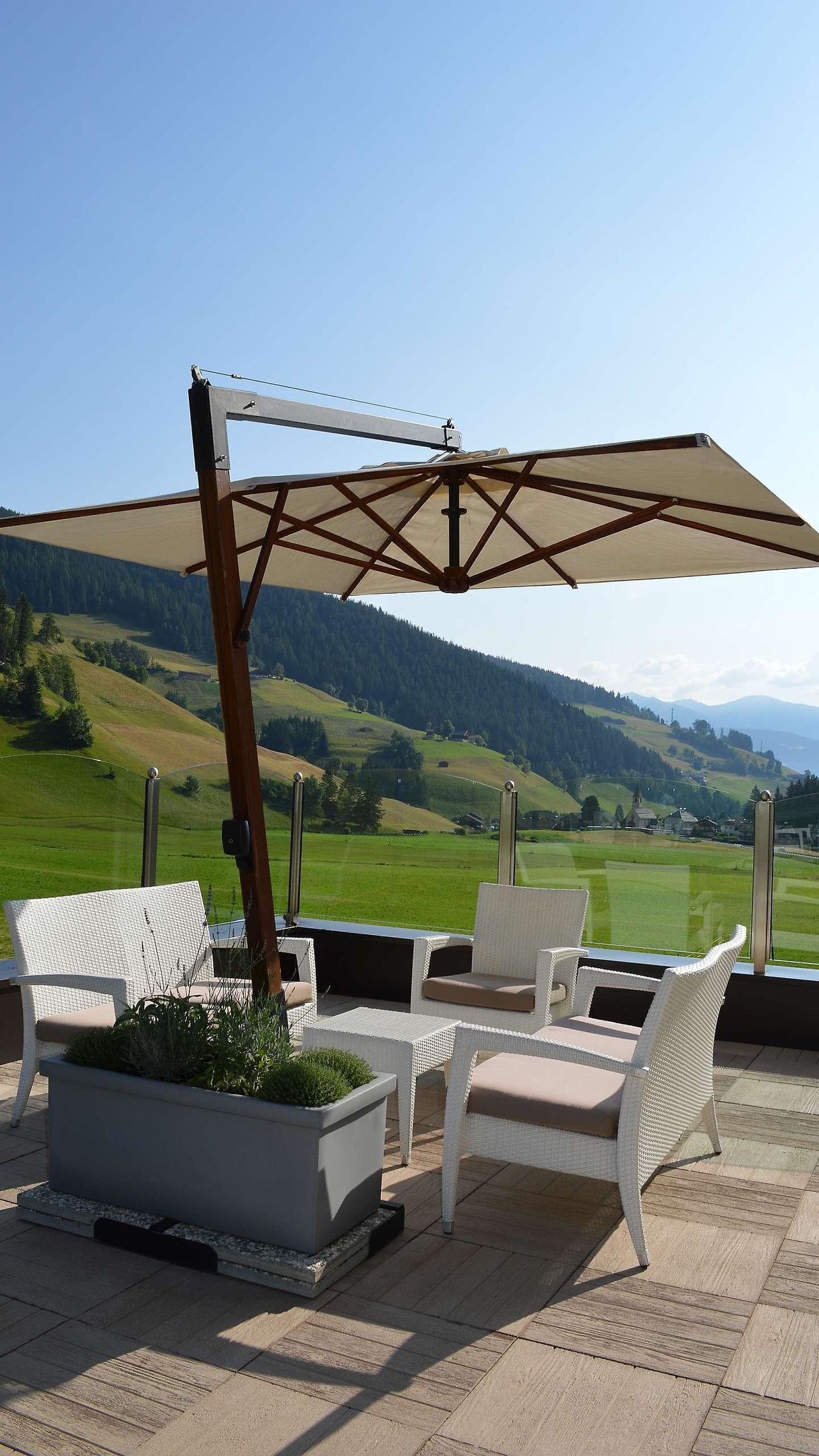 A patio with white wicker furniture, a large umbrella, and a view of green hills and mountains.