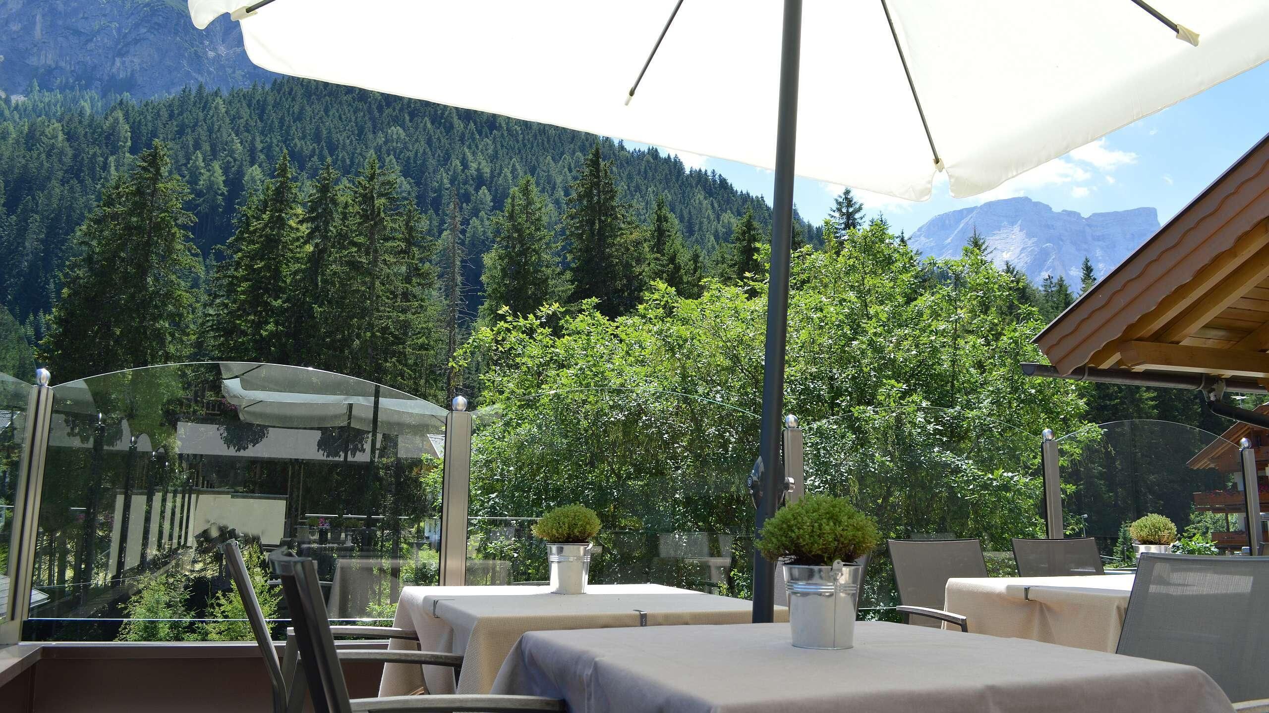 Un espace de restauration en plein air avec des tables et des chaises, un grand parasol et une vue sur une chaîne de montagnes boisée.