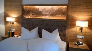 Une chambre à coucher avec un grand lit, deux tables de chevet, un tableau représentant un paysage de montagne accroché au mur, et deux lampes fixées au mur.