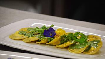 A plate of ravioli with a green sauce and garnished with a purple flower and green leaves.