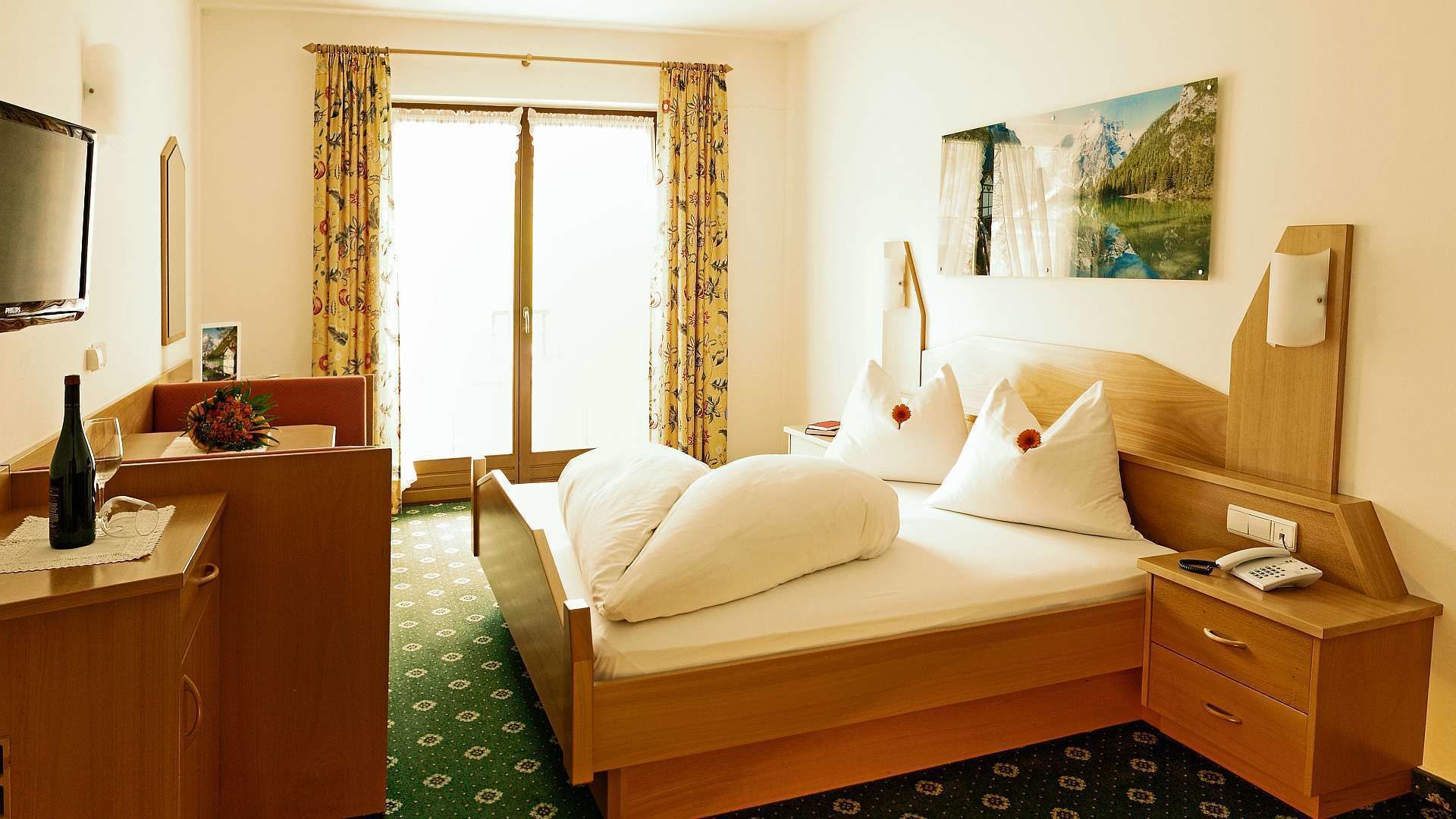 A hotel room with a bed, a desk, a chair, a telephone, and a painting on the wall.
