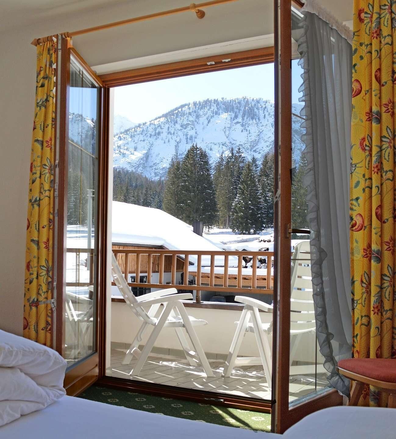 Una habitación con un amplio ventanal corredero que da a un balcón con vistas a montañas cubiertas de nieve y una terraza de madera.