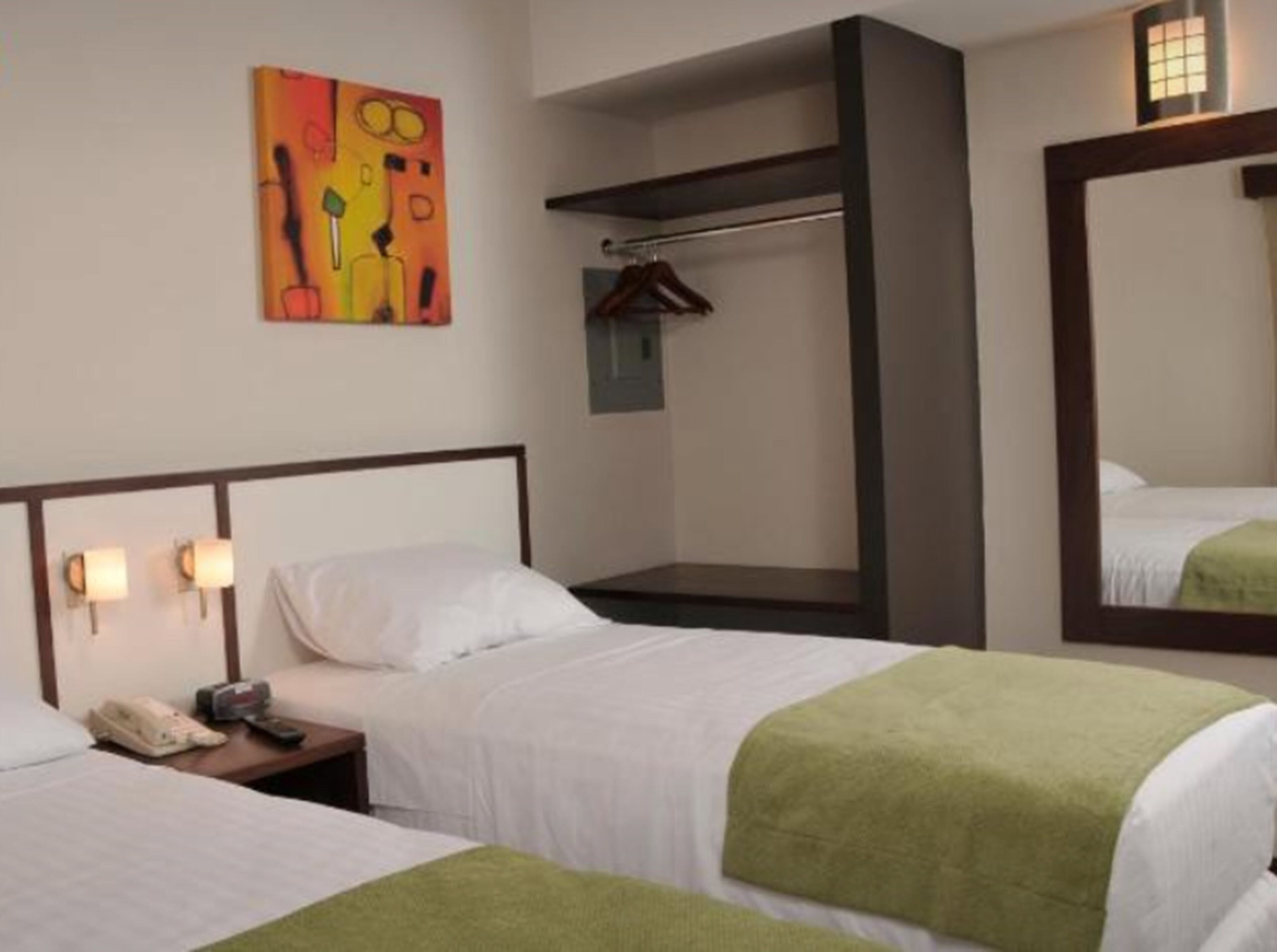 Een hotelkamer met twee bedden, een nachtkastje met een telefoon, een spiegel aan de muur en een kleurrijk abstract schilderij.