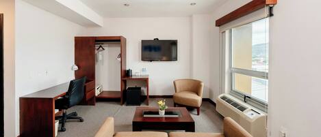 Habitación de hotel moderna con sofá, escritorio, silla, televisor y ventana con vistas.