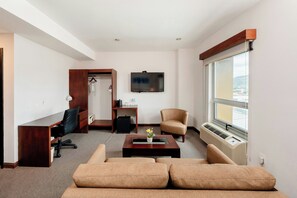 Quarto de hotel moderno com sofá, escrivaninha, cadeira, televisão e janela com vista.