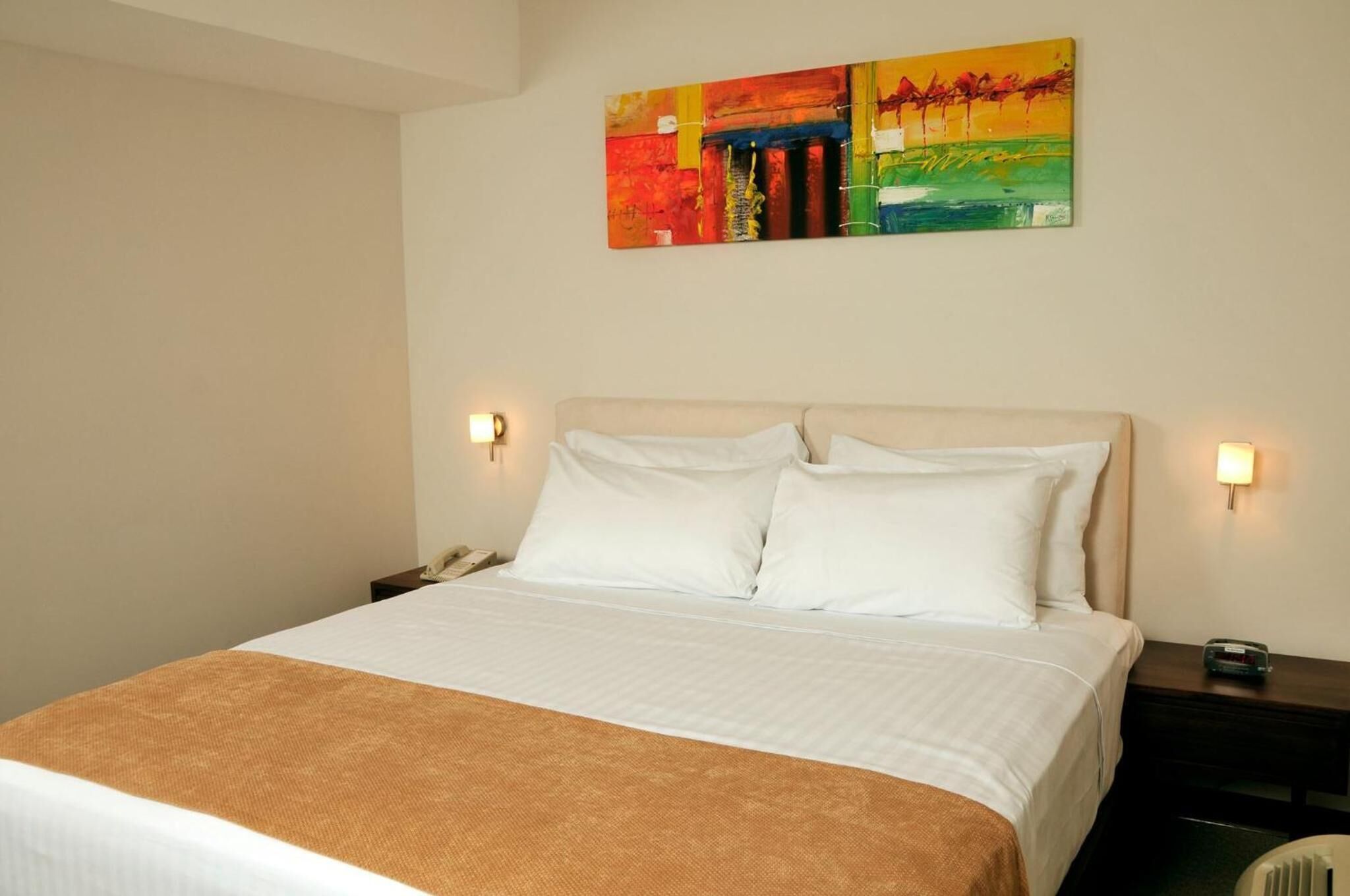 Una habitación de hotel con una cama grande, dos mesitas de noche y un cuadro abstracto de colores en la pared.