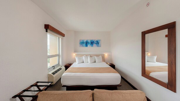 Habitación de hotel con cama, mesitas de noche, ventana, radiador, una obra de arte colgada en la pared y un espejo grande.