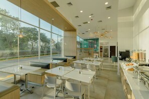 Un café moderno con amplios ventanales, mesas blancas y una zona de bufé.