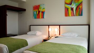 Une chambre d’hôtel avec deux lits, des couvertures vertes, une tête de lit en bois et deux tableaux abstraits accrochés au mur.