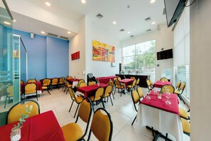 Uma sala de jantar com mesas e cadeiras, uma janela grande e um quadro na parede.