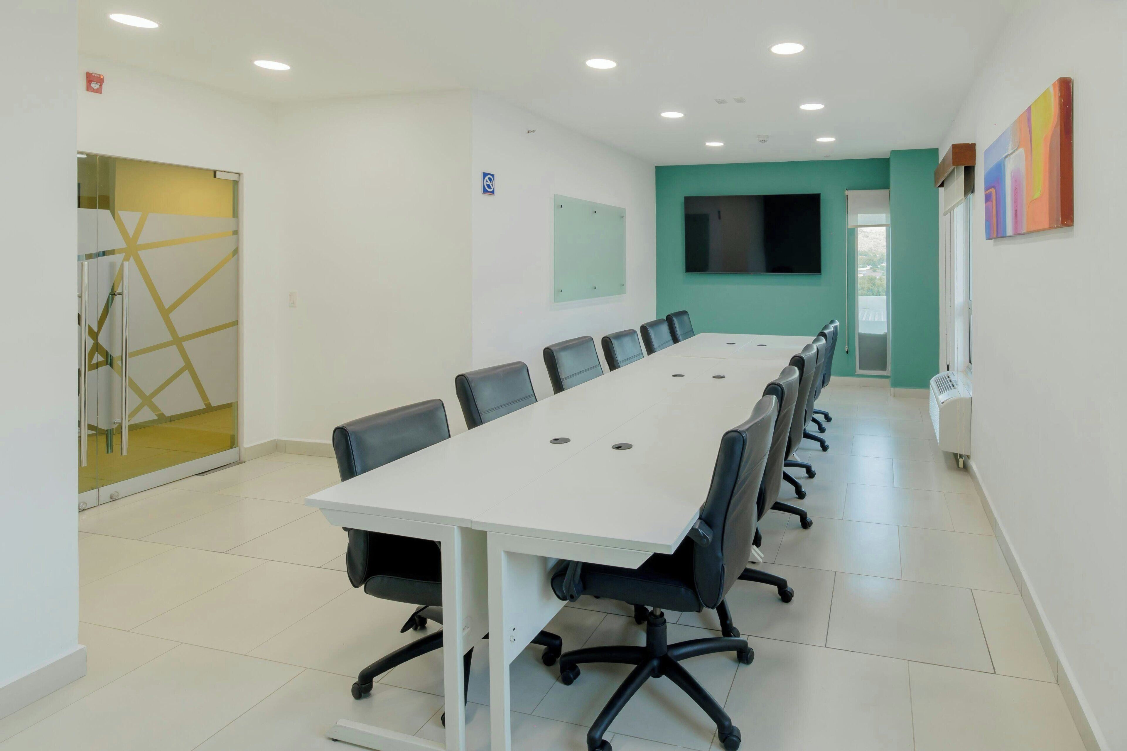 A conference room with a long table, chairs, a TV screen, and a glass partition.