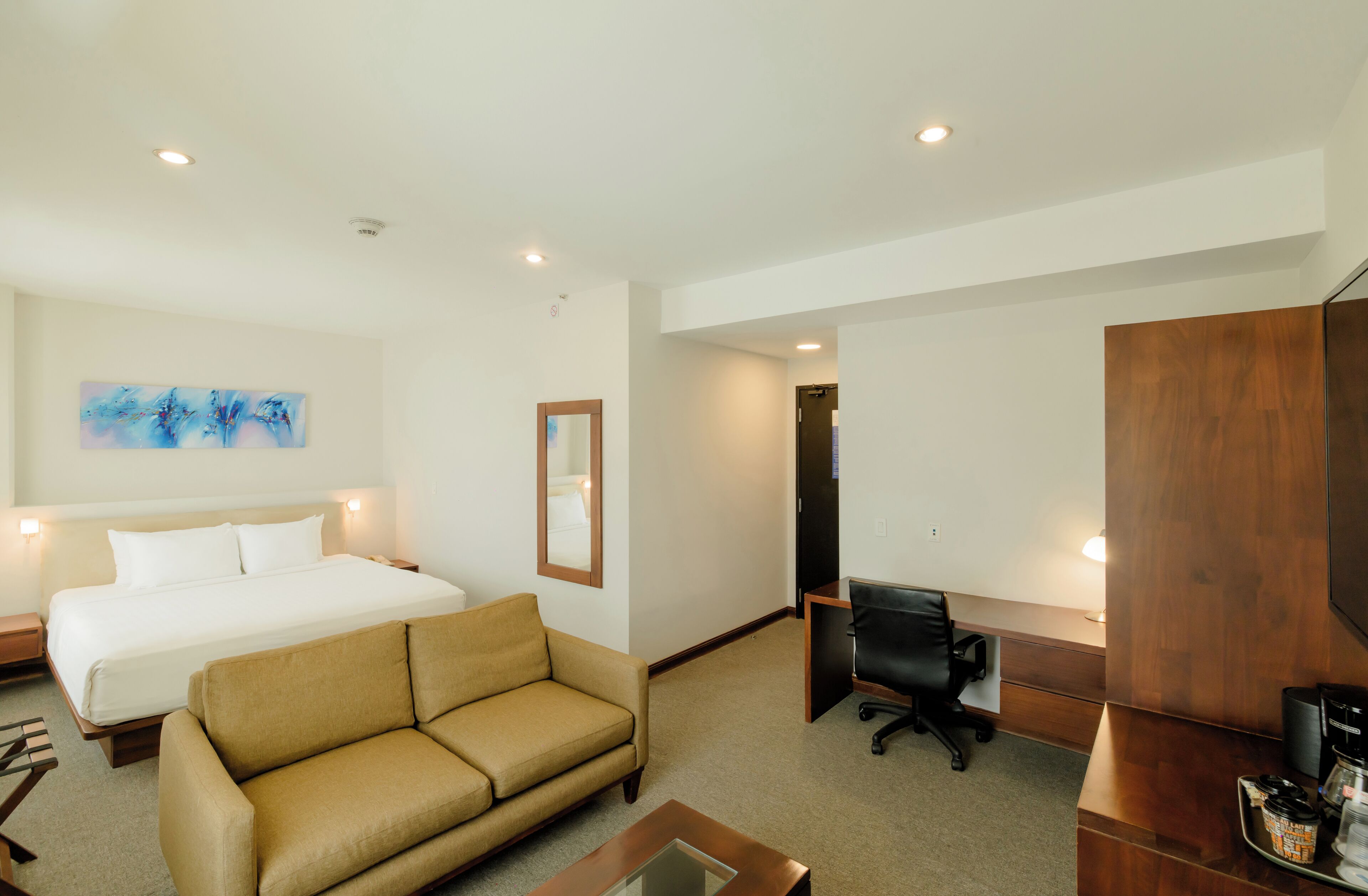 A hotel room with a bed, a sofa, a desk with a chair, a television, and a coffee machine.