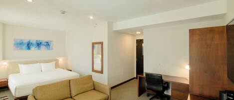 A hotel room with a bed, a sofa, a desk with a chair, a television, and a coffee machine.