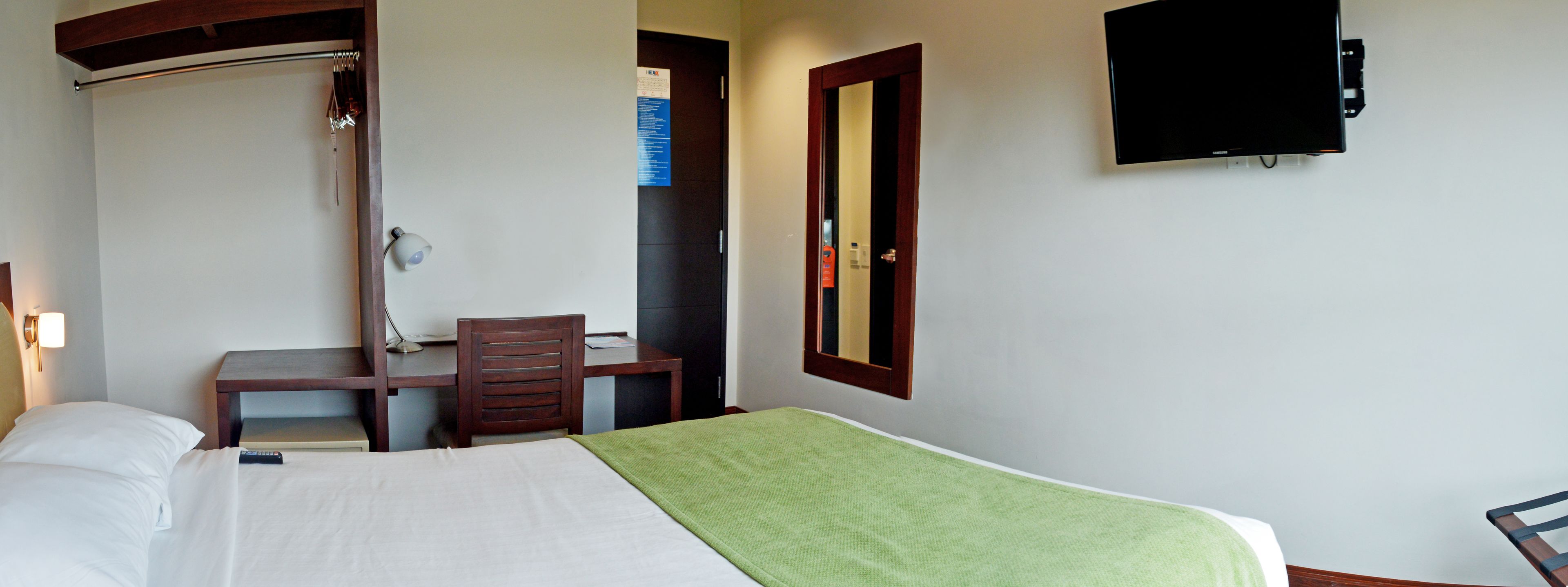 A hotel room with a bed, a desk, a chair, a TV, and a mirror.