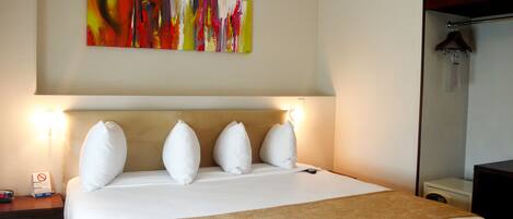 A hotel room with a large bed, a headboard, a bedside table with a lamp, a nightstand, a wall-mounted artwork, and a closet with a hanging rod.