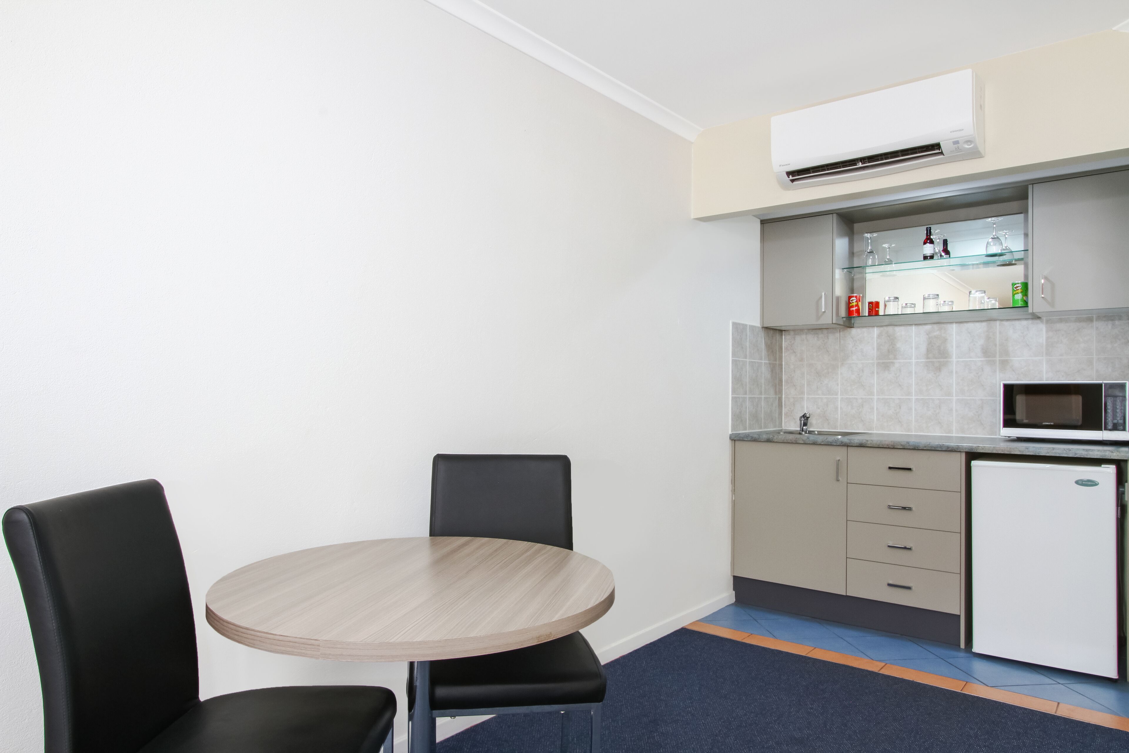 Una cocina compacta con una mesa redonda y dos sillas, un microondas y un refrigerador.