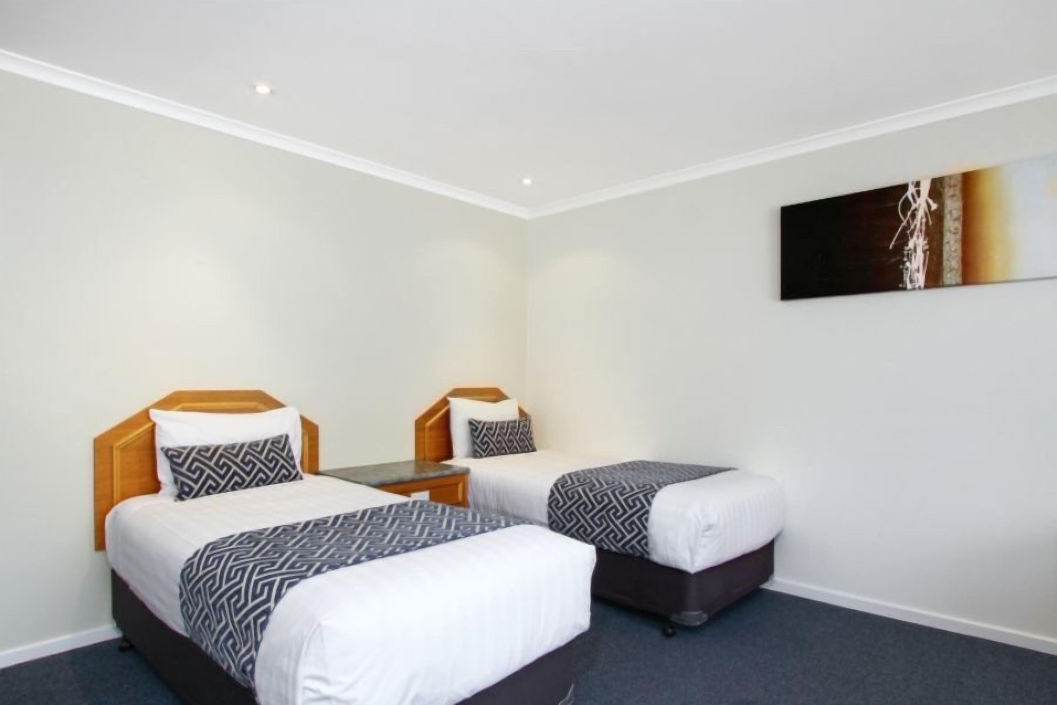 Una habitación de hotel con dos camas, una mesita y un cuadro en la pared.
