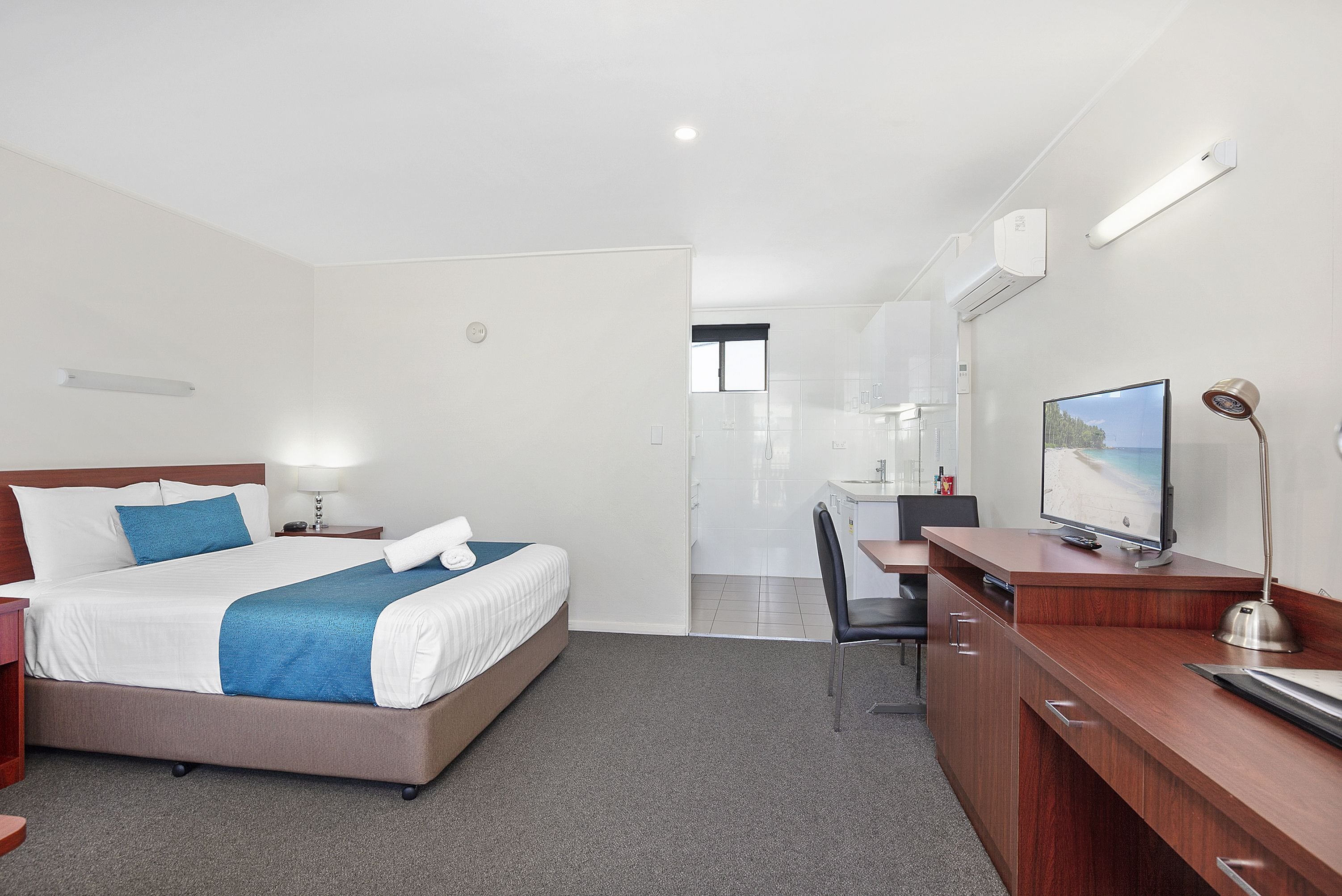 A hotel room with a bed, desk, chair, TV, and a bathroom visible through an open door.