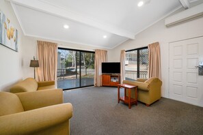 A room with a TV, two sofas, a small table, and a sliding glass door to the outside. - Thunderbird Motel (Yass)