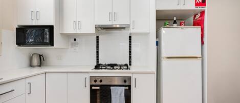 A modern kitchen with white cabinets, a microwave, a stove, and a refrigerator.