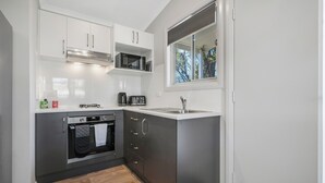 A compact kitchen with a built-in oven, microwave, and sink. - Thunderbird Motel (Yass)