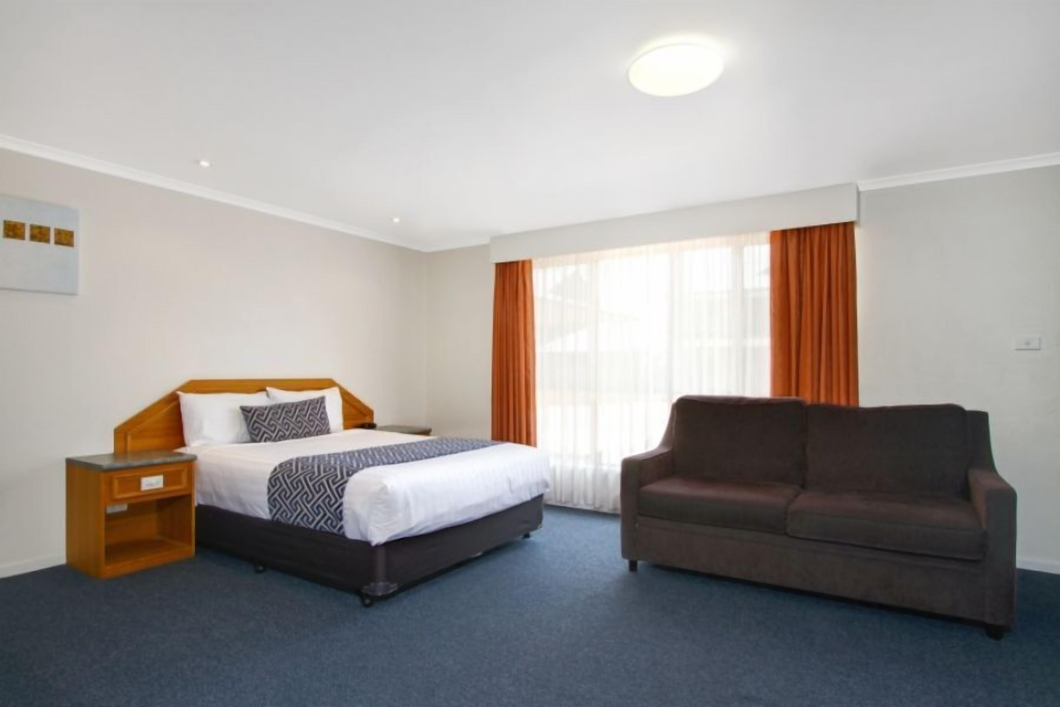 A hotel room with a bed, a sofa, a nightstand, and a window with curtains.
