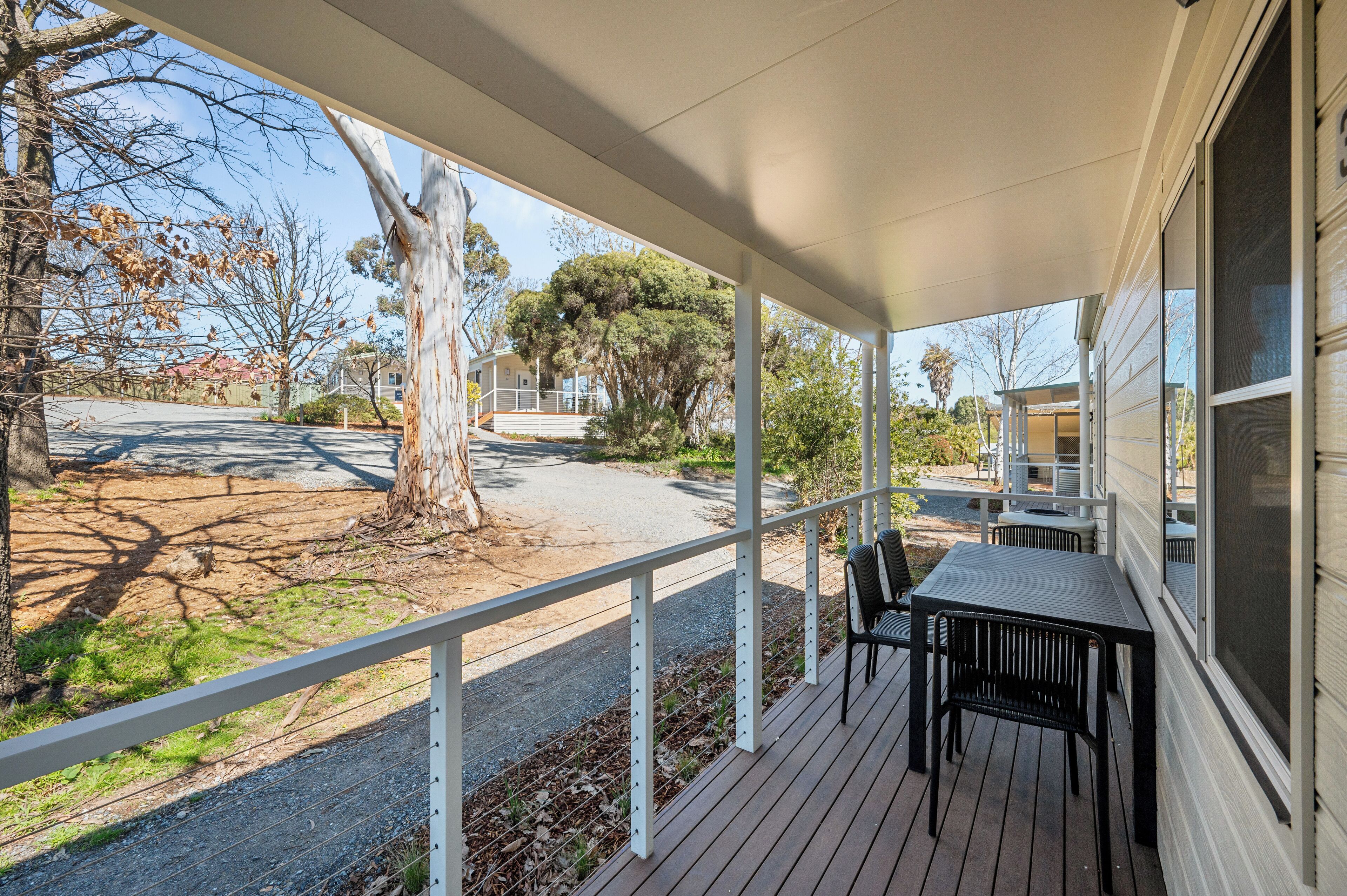 A covered outdoor area with a table and chairs, a tree, and a view of the street.