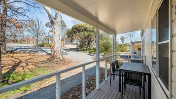 A covered outdoor area with a table and chairs, a tree, and a view of the street.