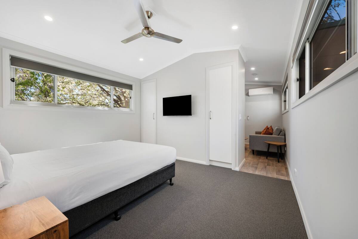 Ein modernes Schlafzimmer mit Bett, Deckenventilator, Fernseher und Blick ins Freie.