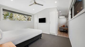 Un dormitorio moderno con cama, ventilador de techo, televisión y vistas al exterior.