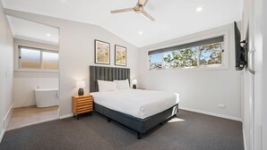 A modern bedroom with a bed, bedside tables, a ceiling fan, a window with a view, and a built-in bench. - Thunderbird Motel (Yass)