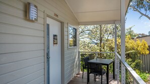 A covered outdoor area with a table and chairs, a door with a number plate, and a view of trees and a fence. - Thunderbird Motel (Yass)