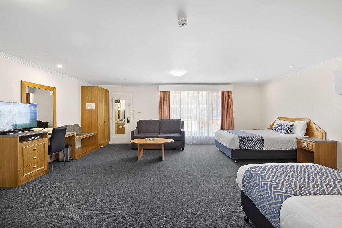 Ein Hotelzimmer mit Schreibtisch, Stuhl, Sofa und zwei Einzelbetten sowie einem Fernseher.