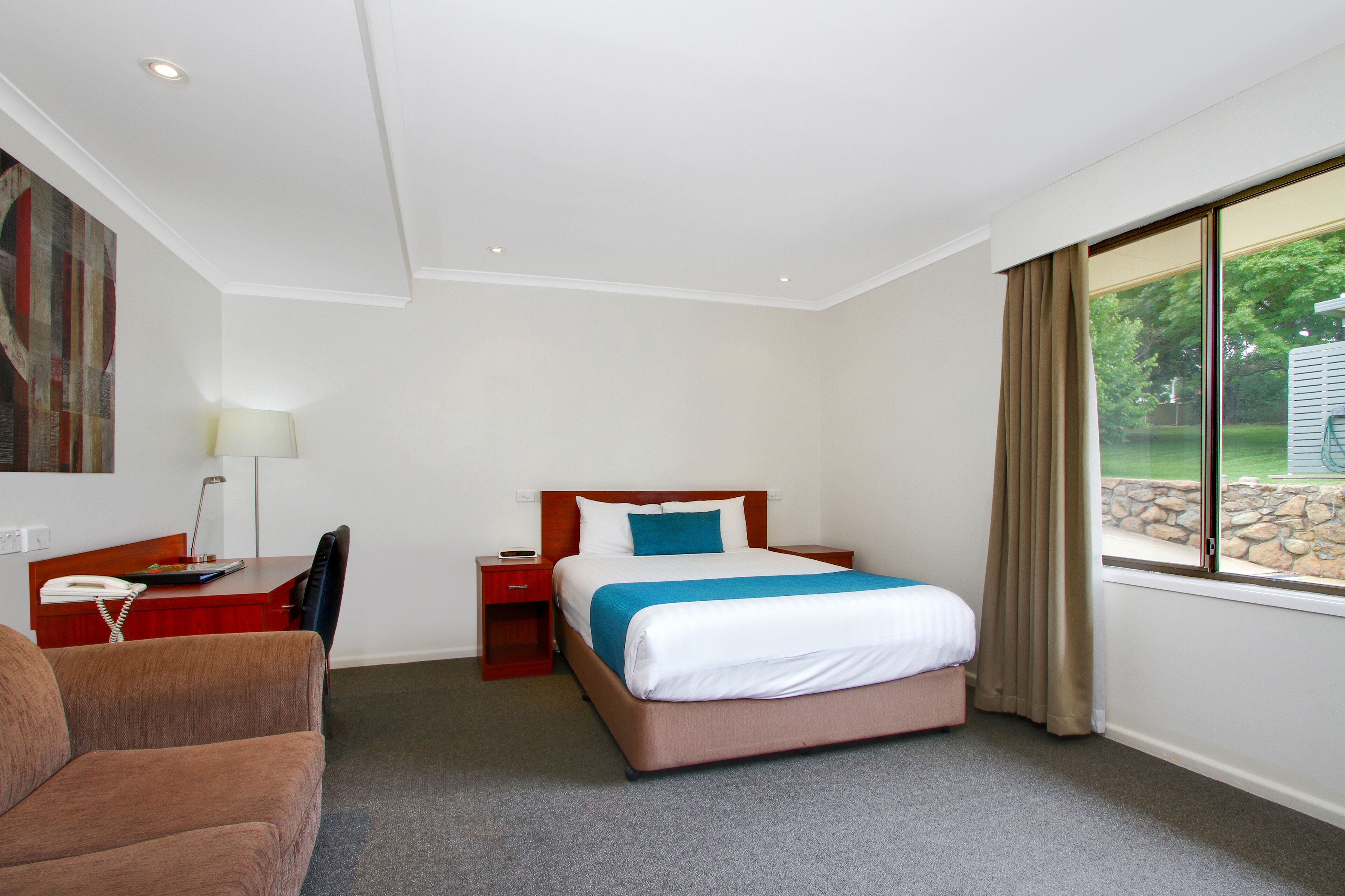 Ein Hotelzimmer mit Bett, Schreibtisch, Stuhl, Lampe und einem Fenster mit Vorhängen.
