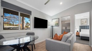 A modern hotel room with a glass dining table, grey sofa, and a flat-screen TV mounted on the wall. - Thunderbird Motel (Yass)