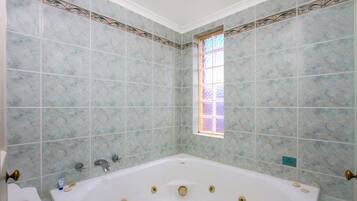 Un baño con una bañera grande, paredes de azulejos, una ventana y una zona de ducha.