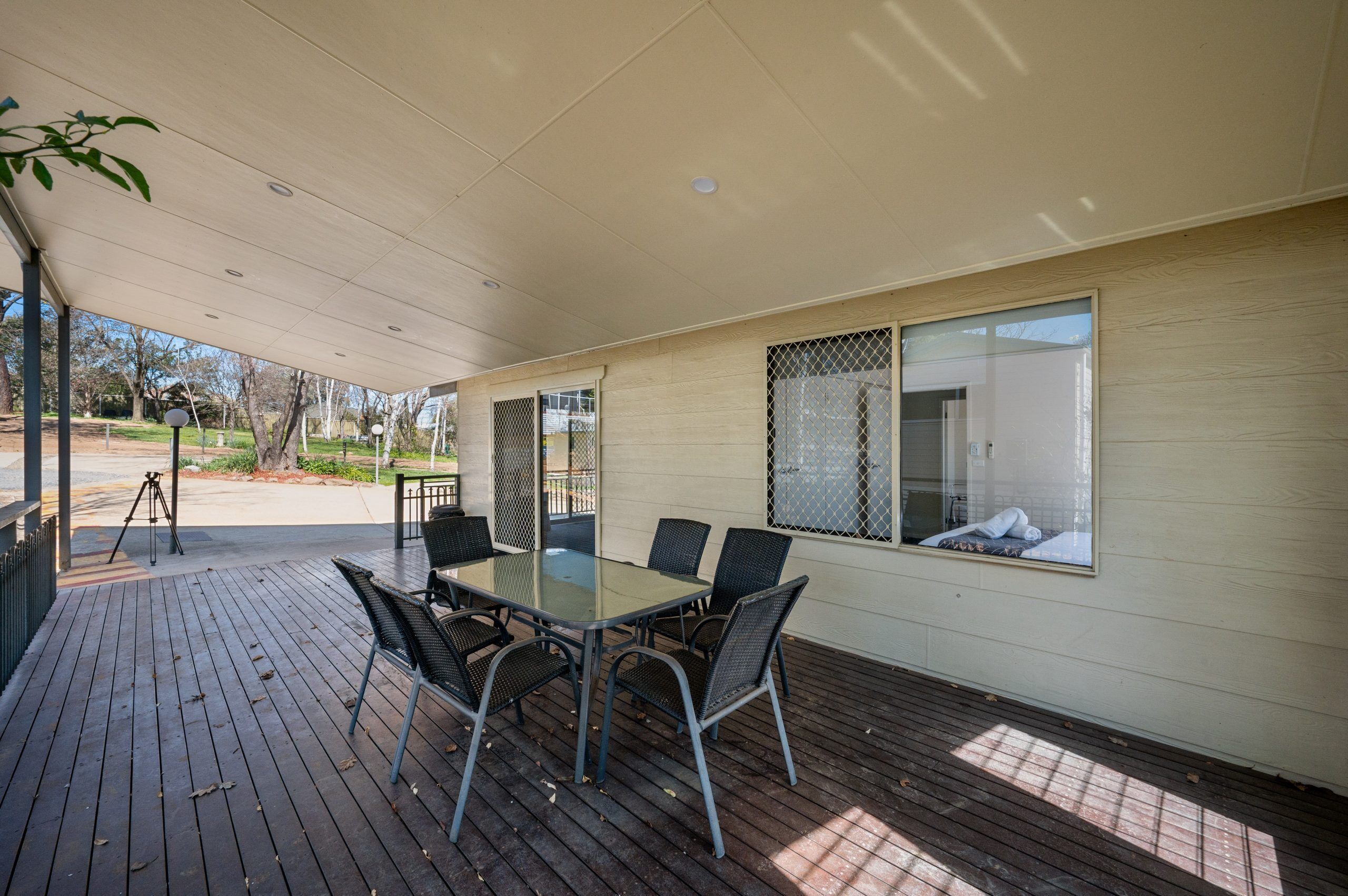 A covered patio with a glass-top table and chairs, a view of the outdoors, and a window with a mesh screen.
