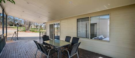 A covered patio with a glass-top table and chairs, a view of the outdoors, and a window with a mesh screen.