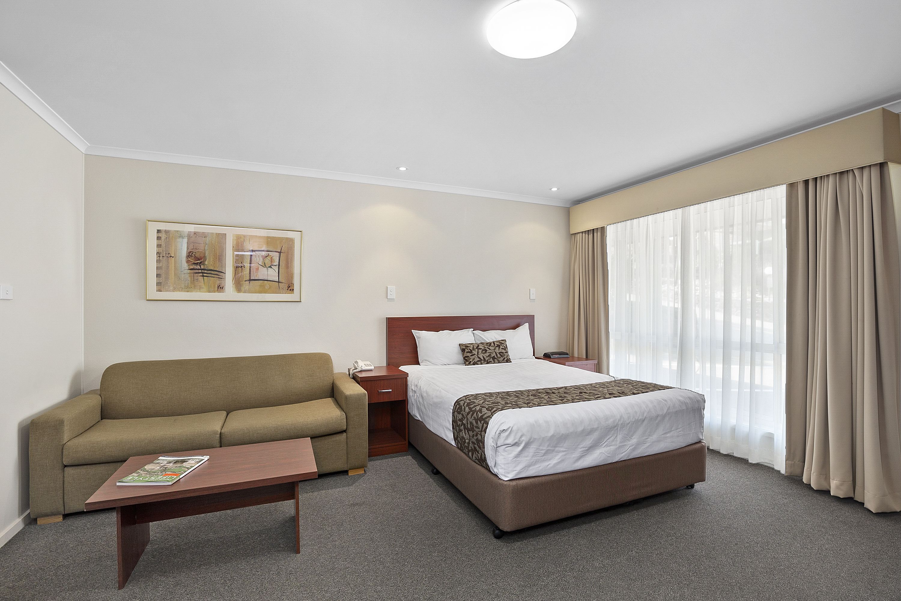 Una habitación de hotel con una cama, un sofá, una mesita de café y un cuadro en la pared.