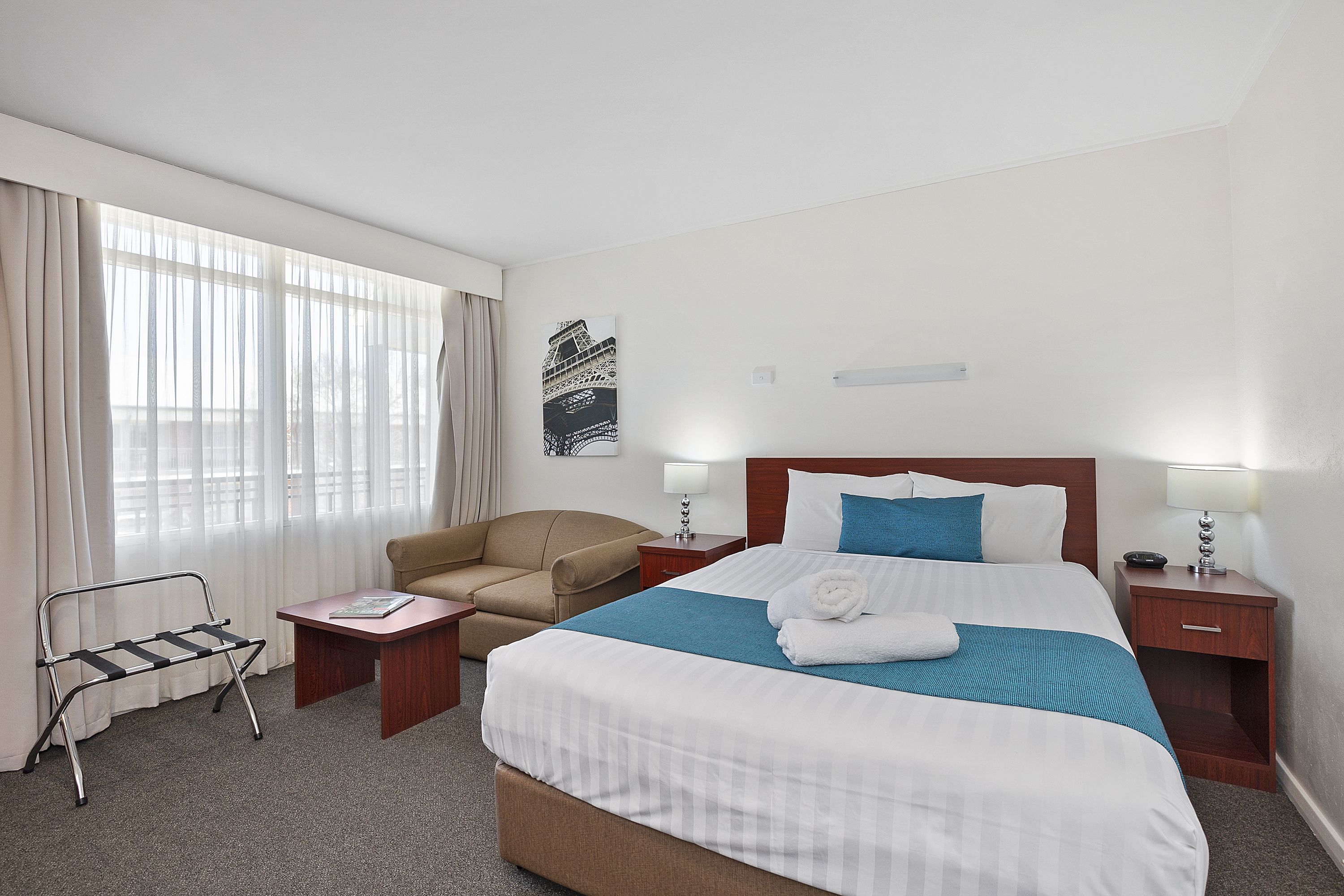 Una habitación de hotel con una cama grande, una silla, una mesita y una ventana con cortinas.