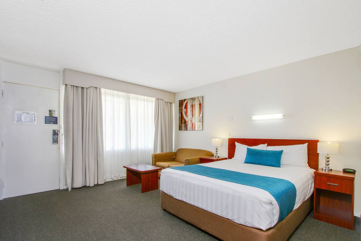 Ein Hotelzimmer mit einem großen Bett, einem Sessel, einem Schreibtisch und einem Nachttisch.