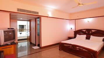 A hotel room with a wooden bed, a television on a wooden cabinet, and a ceiling fan.