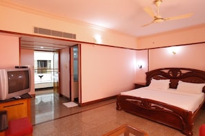 A hotel room with a wooden bed, a television on a wooden cabinet, and a ceiling fan.